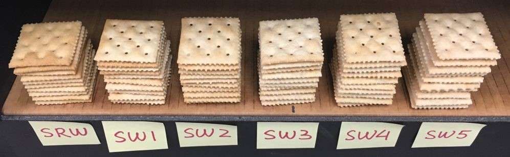 Six stacks of square crackers are lined up on a table, each stack labeled with a sticky note reading SRW, SW1, SW2, SW3, SW4, and SW5. The crackers appear slightly different in color and texture.