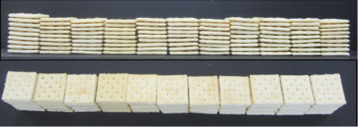 Two rows of stacked square crackers are shown on a black surface. The top row displays the crackers edges, while the bottom row shows the crackers flat, dotted tops.